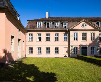 Schloss und Schlossgarten Schwetzingen - Garten - Gesandtenhaus (ehemaliges Prinzenhaus) / Amtsgericht - Von Südost - Blick vom Weg zum nördlichen Zirkelbau auf den südlichen Teil der Südostfassade und das Portal des Gesandtenhauses; links die Rückseite des mittleren Pavillons des nördlichen Zirkelbaus  (Nutzung: Wohnungen für Angehörige der kurfürstlichen Familie, ausländische Besucher, Nicolas de Pigage (1723-1796), Friedrich Ludwig Skell (1750-1823), Johann Michael Zeyher (1770-1843), Sterbeort von Johann Peter Hebel (1760-1826), ab 1805 Amtsgericht) (Bau: Länge x Breite: ca. 40 x 17 Meter; Bauzeit: um 1723; Architekt: unbekannt) (aufgenommen im Juli 2024, am Vormittag)