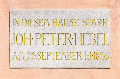 Schloss und Schlossgarten Schwetzingen - Garten - Gesandtenhaus (ehemaliges Prinzenhaus) / Amtsgericht - Von Südost - Blick auf die Gedenktafel zum Tod von Johann Peter Hebel (1760-1826) über dem Eingang des Amtsgerichts; Text der Inschrift: "IN DIESEM HAUSE STARB / JOH . PETER . HEBEL / AM 22 . SEPTEMBER I . J . 1826" (Nutzung: Wohnungen für Angehörige der kurfürstlichen Familie, ausländische Besucher, Nicolas de Pigage (1723-1796), Friedrich Ludwig Skell (1750-1823), Johann Michael Zeyher (1770-1843),  Sterbehaus von Johann Peter Hebel (1760-1826), ab 1805 Amtsgericht) (Bau: Länge x Breite: ca. 40 x 17 Meter; Bauzeit: um 1723; Architekt: unbekannt) (aufgenommen im Juli 2024, am Vormittag)