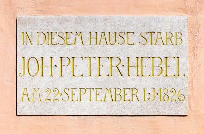 Schloss und Schlossgarten Schwetzingen - Garten - Gesandtenhaus (ehemaliges Prinzenhaus) / Amtsgericht - Von Südost - Blick auf die Gedenktafel zum Tod von Johann Peter Hebel (1760-1826) über dem Eingang des Amtsgerichts; Text der Inschrift: "IN DIESEM HAUSE STARB / JOH . PETER . HEBEL / AM 22 . SEPTEMBER I . J . 1826" (Nutzung: Wohnungen für Angehörige der kurfürstlichen Familie, ausländische Besucher, Nicolas de Pigage (1723-1796), Friedrich Ludwig Skell (1750-1823), Johann Michael Zeyher (1770-1843), Sterbehaus von Johann Peter Hebel (1760-1826), ab 1805 Amtsgericht) (Bau: Länge x Breite: ca. 40 x 17 Meter; Bauzeit: um 1723; Architekt: unbekannt) (aufgenommen im Juli 2024, am Vormittag) Schloss und Schlossgarten Schwetzingen - Garten - Gesandtenhaus (ehemaliges Prinzenhaus) / Amtsgericht - Von Südost - Blick auf die Gedenktafel zum Tod von Johann Peter Hebel (1760-1826) über dem Eingang des Amtsgerichts; Text der Inschrift: "IN DIESEM HAUSE STARB / JOH . PETER . HEBEL / AM 22 . SEPTEMBER I . J . 1826" (Nutzung: Wohnungen für Angehörige der kurfürstlichen Familie, ausländische Besucher, Nicolas de Pigage (1723-1796), Friedrich Ludwig Skell (1750-1823), Johann Michael Zeyher (1770-1843), Sterbehaus von Johann Peter Hebel (1760-1826), ab 1805 Amtsgericht) (Bau: Länge x Breite: ca. 40 x 17 Meter; Bauzeit: um 1723; Architekt: unbekannt) (aufgenommen im Juli 2024, am Vormittag)