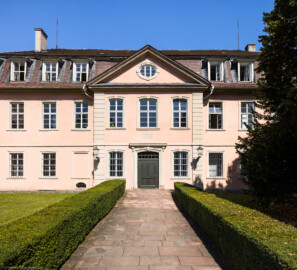 Schloss und Schlossgarten Schwetzingen - Garten - Gesandtenhaus (ehemaliges Prinzenhaus) / Amtsgericht - Von Südost - Blick von der Zeyherstraße auf die Südostfassade und das Portal des Gesandtenhauses  (Nutzung: Wohnungen für Angehörige der kurfürstlichen Familie, ausländische Besucher, Nicolas de Pigage (1723-1796), Friedrich Ludwig Skell (1750-1823), Johann Michael Zeyher (1770-1843), Sterbeort von Johann Peter Hebel (1760-1826), ab 1805 Amtsgericht) (Bau: Länge x Breite: ca. 40 x 17 Meter; Bauzeit: um 1723; Architekt: unbekannt) (aufgenommen im Juli 2024, am späten Vormittag)