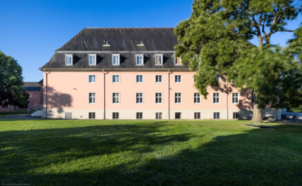 Schloss und Schlossgarten Schwetzingen - Garten - Schlosstheater - Von Norden - Blick vom Gesandtenhausgarten nach Süden auf die Nordfassade des Theaterbaus; die rechten 7 Fenster der Fassade gehören zur Seitenbühne; hinter der Wand links davon befindet sich das Foyer und Treppenhaus, dahinter der Zuschauerrraum; ganz links zwei Schnurbäume und ganz rechts ein Schnurbaum  (Sophora japonica, links Baum-Nr. 72 und 73, rechts Baum-Nr. 85) (Gesamter Bau: Länge x Breite: ca. 62 x 35 Meter; Architekt: Nicolas de Pigage (1723-1796); Bauzeit: 1752-1753, Erweiterung 1762, Sanierung: 1937, Renovierung: 1952, Generalsanierung / Umbau 1971-1974, Restaurierung: 1999-2005) (aufgenommen im Juli 2024, am frühen Vormittag)