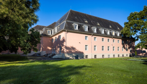 Schloss und Schlossgarten Schwetzingen - Garten - Schlosstheater - Von Nordost - Blick vom Gesandtenhausgarten nach Südwest auf die Ostfassade (links) und Nordfassade (rechts) des Theaterbaus; die rechten 7 Fenster der Nordfassade gehören zur Seitenbühne; hinter der Wand links davon befindet sich das Foyer und Treppenhaus, dahinter der Zuschauerrraum; die erste Treppe bzw. die erste Tür von rechts führt in das nördliche Treppenhaus, die Treppe links davon bzw. die nächsten beiden Türen führen in das Foyer, die Treppe links davon bzw. die Tür führt in das Vestibül; ganz links zwei Schnurbäume und ganz rechts ein Schnurbaum  (Sophora japonica, links Baum-Nr. 72 und 73, rechts Baum-Nr. 85) (Gesamter Bau: Länge x Breite: ca. 62 x 35 Meter; Architekt: Nicolas de Pigage (1723-1796); Bauzeit: 1752-1753, Erweiterung 1762, Sanierung: 1937, Renovierung: 1952, Generalsanierung / Umbau 1971-1974, Restaurierung: 1999-2005) (aufgenommen im Juli 2024, am Vormittag)