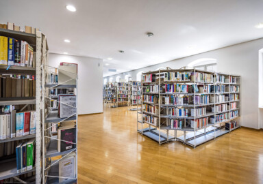 Schloss und Schlossgarten Schwetzingen - Garten - Invalidenkaserne (ehemaliges Baumagazin) / Stadtbibliothek  - Südflügel - Von innen - Erdgeschoss - Von Westen - Blick nach Osten in den Bibliotheksraum des Südflügels (Vierflügelanlage: Länge x Breite: ca. 60 x 50 Meter; Ostflügel: ca. 60 x 10 Meter; Bauzeit: um 1774; Architekt des Baummagazins: Nicolas de Pigage; Umbau zur Kaserne: Ingenieur-Oberst von Pfister) (aufgenommen im Juli 2024, um die Mittagszeit)