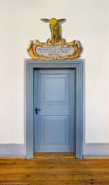 Schloss und Schlossgarten Schwetzingen - Schloss - Südflügel / Hofdamenflügel - Querbau - Von Innen - Obergeschoss - Gang - Ostwand - 4. Gemälde von Norden - Von Westen - Blick auf eine Tür mit einer "Hirschkartusche" oberhalb des Türrahmens; Gemälde zur Erinnerung an eine Jagd; Inschrift: "Den 5. Septembr 1719 haben Ihro / Churfürstl. Durchl. diesen Hirsch /  von 14 Endten im Kholler / geschossen"; Datierung: wohl unter dem Kurfürsten Karl III. Philipp (1661-1742, reg. 1716-1742); Malerei in Fresco-Technik; Oval im Stirnbereich des Hirsches diente der Anbringung des Hirschgeweihs; Malerei vermutlich in jüngerer Zeit überstrichen  (Südflügel: L-förmig, Länge x Breite Längsbau ca. 50 x 14 Meter, Querbau ca. 15 x 11 Meter,; Architekt: Johann Adam Breunig (1660-1727); Fertigstellung: 1710, letzte Renovierung: 2009-2012) (aufgenommen im August 2024, am frühen Nachmittag)