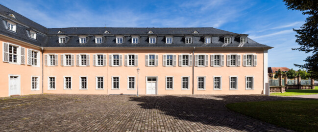 Schloss und Schlossgarten Schwetzingen - Schloss - Südflügel / Hofdamenflügel - Längsbau - Von Süden - Blick auf die komplette Südfassade und das südliche Hauptportal des Längsbaus; links die Ostseite des Querbaus des Küchenflügels; rechts ein Ende des Gitterzauns um den Ehrenhof des Schlosses (Südflügel: L-förmig, Länge x Breite Längsbau ca. 50 x 14 Meter, Querbau ca. 15 x 11 Meter; Architekt: Johann Adam Breunig (1660-1727); Fertigstellung: 1710, letzte Renovierung: 2009-2012) (aufgenommen im August 2024, am späten Vormittag)