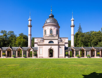 Schloss und Schlossgarten Schwetzingen - Garten - Moschee - Von außen - Von Osten - Blick vom östlichen Portalbau des Kreuzgangs nach Westen auf die Moschee mit den beiden Minaretten und auf den türkischen Garten mit dem Kreuzgang; in der Mitte das Hauptgebäude mit der Eingangshalle, über dem Kubus der Tambour und die Kuppel (Moschee: Länge mit Minaretten und Verbindungsbau zum Kreuzgang ca. 44 Meter, Breite ca. 29 Meter; Bauzeit: 1782-1795; Architekt: Nicolas de Pigage; Gesamtrestaurierung Moscheeanlage: ca. 1995 bis 2007) (aufgenommen im August 2024, am späten Vormittag)