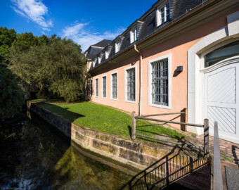 Schloss und Schlossgarten Schwetzingen - Schloss - Küchenflügel / Küchenbau - Längsbau, Südseite - Von Südost - Blick von der kleinen Brücke zum südlichen Eingang auf den westlichen Teil des Längsbaus; links der Leimbachkanal (Küchenflügel: L-förmig, Länge x Breite Längsbau ca. 75 x 13 Meter, Querbau ca. 25 x 11 Meter; Architekt: Nicolas de Pigage (1723-1796); Fertigstellung: 1761, letzte Renovierung: 2009-2012) (aufgenommen im August 2024, am Vormittag)