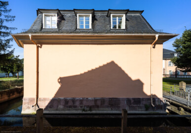 Schloss und Schlossgarten Schwetzingen - Schloss - Küchenflügel / Küchenbau - Längsbau - Von Osten - Blick vom Dozentenhaus nach Westen auf die Ostfassade des Längsbau; links und vorne unten der Leimbachkanal; rechts eine kleine Brücke über den Leimbach; ganz rechts im Hintergrund die Ostfassade des Längsbau des Südflügels (Küchenflügel: L-förmig, Länge x Breite Längsbau ca. 75 x 13 Meter, Querbau ca. 25 x 11 Meter; Architekt: Nicolas de Pigage (1723-1796); Fertigstellung: 1761, letzte Renovierung: 2009-2012) (aufgenommen im August 2024, am Vormittag)