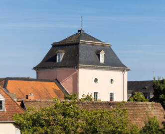 Schloss und Schlossgarten Schwetzingen - Sonstige Bauten - Oberes Wasserwerk - Wasserturm - Von außen - Von Nordwest - Blick vom Dachgeschoss des Gesandtenhauses / Amtsgerichts auf den Wasserturm des Oberen Wasserwerks; im Dachgeschoss in 18 Meter Höhe befanden sich zwei Wasserbehälter aus Blei, im Obergeschoss in 10 Meter Höhe zwei kleinere Reservoirs  (Gesamte Anlage Brunnenstube, Pumpenstube, Räderwerk, Wasserturm und Kühlhaus): Länge x Breite: ca. 30 x 29 Meter, Wasserturm: Länge x Breite: ca. 14 x 14 Meter, Firsthöhe ca. 24 Meter; Bauzeit Anlage: um 1774, Gesamtinstandsetzung: 1994–2000; Architekt: Nicolas de Pigage, Brunnenmeister: Thomas Breuer) (aufgenommen im August 2024, am späten Nachmittag)
