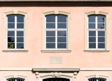 Schloss und Schlossgarten Schwetzingen - Garten - Gesandtenhaus (ehemaliges Prinzenhaus) / Amtsgericht - Von Südost -  Blick auf die drei Fenster im Obergeschoss des Mittelrisalits (Nutzung: Wohnungen für Angehörige der kurfürstlichen Familie, ausländische Besucher, Nicolas de Pigage (1723-1796), Friedrich Ludwig Skell (1750-1823), Johann Michael Zeyher (1770-1843), Sterbeort von Johann Peter Hebel (1760-1826), ab 1805 Amtsgericht) (Bau: Länge x Breite: ca. 40 x 17 Meter; Bauzeit: um 1723; Architekt: unbekannt) (aufgenommen im August 2024, am späten Vormittag)
