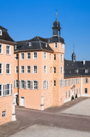 Schloss und Schlossgarten Schwetzingen - Schloss - Mittelbau - Hofseite - Von Südost - Blick vom Dachgeschoss des Südflügels nach Nordwesten auf den Ehrenhof, den Mittelbau und den Nordflügel (Hofkavaliersflügel); in der Bildmitte das nördliche Treppenhaus, rechts davon der Nordturm, rechts davon der Querbau des Nordflügels mit der Schlosskapelle und ganz rechts der Längsbau des Nordflügels (heute vom Finanzamt genutzt) (Mittelbau: Länge Westseite ca. 45 Meter, Breite Süd-/Nordseite ca. 38 Meter; Wiederaufbau / Erweiterung: 1698-1717; Architekt: Johann Adam Breunig) (aufgenommen im August 2024, am späten Vormittag)