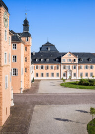 Schloss und Schlossgarten Schwetzingen - Schloss - Mittelbau / Nordflügel - Von Süden - Blick vom Dachgeschoss des Südflügels nach Norden auf den Ehrenhof, den Mittelbau und den Nordflügel (den Hofkavaliersflügel, heute vom Finanzamt genutzt); v.l.n.r.: Südturm mit Uhr, nördliches Treppenhaus, Nordturm, Querbau des Nordflügels mit der Schlosskapelle, Längsbau des Nordflügels; im Hintergrund das Dach des Oberen Wasserwerks (Mittelbau: Länge Westseite ca. 45 Meter, Breite Süd-/Nordseite ca. 38 Meter; Wiederaufbau / Erweiterung: 1698-1717; Architekt: Johann Adam Breunig; NordFlügel: L-förmig, Länge x Breite Längsbau ca. 50 x 14 Meter, Querbau ca. 15 x 12 Meter; Architekt: Johann Adam Breunig (1660-1727); Fertigstellung: 1710) (aufgenommen im August 2024, am Vormittag)