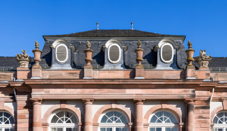 Schloss und Schlossgarten Schwetzingen - Garten - Nördlicher Zirkelbau - Mittlerer Pavillon - Von Südwest - Blick auf den oberen Teil der Südwestfassade sowie auf das Gebälk und den Schmuck (Vasen und Blumenkörbe) (Gesamter Bau: Länge Bogen ca. 175 Meter, Breite zwischen ca. 11 und 18 Meter, 51 Achsen, 5 Pavillons, 4 Zwischenbauten; Architekt: Alessandro Alessandro Galli da Bibiena (1686-1748), Bauleitung: zuerst Guillaume d’Hauberat (1680–1749), dann Nicolas de Pigage (1723-1796); Bauzeit: 1748-1750) (aufgenommen im Oktober 2024, um die Mittagszeit)