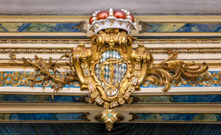 Schloss und Schlossgarten Schwetzingen - Garten - Schlosstheater - Von innen - Proszenium - Blick vom Zuschauerraum auf das geschnitzte kurfürstliche Wappen (mit dem Monogramm "CT" für Carl Theodor, dem Kurhut und einer Ordenskette) sowie Blatt- und Blütenranken in der Mitte des oberen horizontalen Teils des Proszeniumsrahmens (Gesamter Bau: Länge x Breite: ca. 62 x 35 Meter; Architekt: Nicolas de Pigage (1723-1796); Bauzeit: 1752-1753, Erweiterung 1762, Sanierung: 1937, Renovierung: 1952, Generalsanierung / Umbau 1971-1974, Restaurierung: 1999-2005) (aufgenommen im November 2024, am Nachmittag)