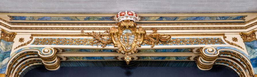 Schloss und Schlossgarten Schwetzingen - Garten - Schlosstheater - Von innen - Proszenium - Blick vom Parkett auf den Architravbalken des Proszeniums mit den beiden Volutenkonsolen; in der Mitte das kurfürstliche Wappen (mit dem Monogramm "CT" für Carl Theodor, dem Kurhut und einer Ordenskette) sowie Blatt- und Blütenranken (Gesamter Bau: Länge x Breite: ca. 62 x 35 Meter; Architekt: Nicolas de Pigage (1723-1796); Bauzeit: 1752-1753, Erweiterung 1762, Sanierung: 1937, Renovierung: 1952, Generalsanierung / Umbau 1971-1974, Restaurierung: 1999-2005) (aufgenommen im Dezember 2024, am Nachmittag) Schloss und Schlossgarten Schwetzingen - Garten - Schlosstheater - Von innen - Proszenium - Blick vom Parkett auf den Architravbalken des Proszeniums mit den beiden Volutenkonsolen; in der Mitte das kurfürstliche Wappen (mit dem Monogramm "CT" für Carl Theodor, dem Kurhut und einer Ordenskette) sowie Blatt- und Blütenranken (Gesamter Bau: Länge x Breite: ca. 62 x 35 Meter; Architekt: Nicolas de Pigage (1723-1796); Bauzeit: 1752-1753, Erweiterung 1762, Sanierung: 1937, Renovierung: 1952, Generalsanierung / Umbau 1971-1974, Restaurierung: 1999-2005) (aufgenommen im Dezember 2024, am Nachmittag)
