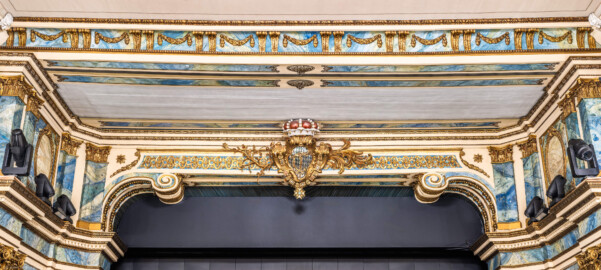 Schloss und Schlossgarten Schwetzingen - Garten - Schlosstheater - Von innen - Proszenium - Blick vom Parterre auf den oberen Abschluss des Proszeniums; in der Mitte der Architravbalken mit den beiden Volutenkonsolen, das kurfürstliche Wappen (mit dem Monogramm "CT" für Carl Theodor, dem Kurhut und einer Ordenskette) sowie Blatt- und Blütenranken; links und rechts ein Teil der korinthischen Pilasterordnung, ganz oben ein verzierter Balken als Übergang zur Decke des Zuschauerraums (Gesamter Bau: Länge x Breite: ca. 62 x 35 Meter; Architekt: Nicolas de Pigage (1723-1796); Bauzeit: 1752-1753, Erweiterung 1762, Sanierung: 1937, Renovierung: 1952, Generalsanierung / Umbau 1971-1974, Restaurierung: 1999-2005) (aufgenommen im Dezember 2024, am Nachmittag) Schloss und Schlossgarten Schwetzingen - Garten - Schlosstheater - Von innen - Proszenium - Blick vom Parterre auf den oberen Abschluss des Proszeniums; in der Mitte der Architravbalken mit den beiden Volutenkonsolen, das kurfürstliche Wappen (mit dem Monogramm "CT" für Carl Theodor, dem Kurhut und einer Ordenskette) sowie Blatt- und Blütenranken; links und rechts ein Teil der korinthischen Pilasterordnung, ganz oben ein verzierter Balken als Übergang zur Decke des Zuschauerraums (Gesamter Bau: Länge x Breite: ca. 62 x 35 Meter; Architekt: Nicolas de Pigage (1723-1796); Bauzeit: 1752-1753, Erweiterung 1762, Sanierung: 1937, Renovierung: 1952, Generalsanierung / Umbau 1971-1974, Restaurierung: 1999-2005) (aufgenommen im Dezember 2024, am Nachmittag)