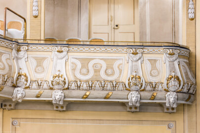 Schloss und Schlossgarten Schwetzingen - Garten - Schlosstheater - Von innen - Balkon - Von Norden - Blick vom Parkett auf die südwestlichste Loge des Balkons und auf die reich verzierte Brüstung; unten ein kannelierter Rundstab, umwunden von einem vergoldeten Band, besetzt mit Löwenmasken, darüber ein Fries mit Akanthusblättern, darüber auf streifigem Grund ein Wellenband, dazwischen balusterartige Blenden mit Voluten, Tuchgehängen und Muscheln, darüber ein Fries aus Kreisen, darüber der Handlauf (Gesamter Bau: Länge x Breite: ca. 62 x 35 Meter; Architekt: Nicolas de Pigage (1723-1796); Bauzeit: 1752-1753, Erweiterung 1762, Sanierung: 1937, Renovierung: 1952, Generalsanierung / Umbau 1971-1974, Restaurierung: 1999-2005) (aufgenommen im Dezember 2024, am Nachmittag) Schloss und Schlossgarten Schwetzingen - Garten - Schlosstheater - Von innen - Balkon - Von Norden - Blick vom Parkett auf die südwestlichste Loge des Balkons und auf die reich verzierte Brüstung; unten ein kannelierter Rundstab, umwunden von einem vergoldeten Band, besetzt mit Löwenmasken, darüber ein Fries mit Akanthusblättern, darüber auf streifigem Grund ein Wellenband, dazwischen balusterartige Blenden mit Voluten, Tuchgehängen und Muscheln, darüber ein Fries aus Kreisen, darüber der Handlauf (Gesamter Bau: Länge x Breite: ca. 62 x 35 Meter; Architekt: Nicolas de Pigage (1723-1796); Bauzeit: 1752-1753, Erweiterung 1762, Sanierung: 1937, Renovierung: 1952, Generalsanierung / Umbau 1971-1974, Restaurierung: 1999-2005) (aufgenommen im Dezember 2024, am Nachmittag)