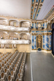 Schloss und Schlossgarten Schwetzingen - Garten - Schlosstheater - Von innen - Zuschauerraum / Südwand / Proszenium - Von Norden - Blick vom Balkon auf der Nordseite nach Süden in den Zuschauerraum, auf die Südwand mit Logen, Balkon und Rang, auf das südliche Proszenium sowie auf den Orchestergraben; der Orchestergraben ist fast auf Höhe der Rampe angehoben; im unteren Teil der Südseite (vom Parkett bis zum Rang) die komposite Pilasterordnung; in der Mitte die Trompeterloge mit Musikinstrumenten (Flöten, Geige, Horn, Laute) und Notenblätter auf einem Gitterwerk sowie auf Girlanden, einem verschlungenen Band, einer Maske und weiteren Verzierungen, unten die Tür zum Orchestergraben; im oberen Teil der Südseite (Rang bis zur Decke) die korinthische Pilasterordnung; rechts oben der Architravbalken mit Volutenkonsolen (Gesamter Bau: Länge x Breite: ca. 62 x 35 Meter; Architekt: Nicolas de Pigage (1723-1796); Bauzeit: 1752-1753, Erweiterung 1762, Sanierung: 1937, Renovierung: 1952, Generalsanierung / Umbau 1971-1974, Restaurierung: 1999-2005) (aufgenommen im Dezember 2024, am frühen Nachmittag) Schloss und Schlossgarten Schwetzingen - Garten - Schlosstheater - Von innen - Zuschauerraum / Südwand / Proszenium - Von Norden - Blick vom Balkon auf der Nordseite nach Süden in den Zuschauerraum, auf die Südwand mit Logen, Balkon und Rang, auf das südliche Proszenium sowie auf den Orchestergraben; der Orchestergraben ist fast auf Höhe der Rampe angehoben; im unteren Teil der Südseite (vom Parkett bis zum Rang) die komposite Pilasterordnung; in der Mitte die Trompeterloge mit Musikinstrumenten (Flöten, Geige, Horn, Laute) und Notenblätter auf einem Gitterwerk sowie auf Girlanden, einem verschlungenen Band, einer Maske und weiteren Verzierungen, unten die Tür zum Orchestergraben; im oberen Teil der Südseite (Rang bis zur Decke) die korinthische Pilasterordnung; rechts oben der Architravbalken mit Volutenkonsolen (Gesamter Bau: Länge x Breite: ca. 62 x 35 Meter; Architekt: Nicolas de Pigage (1723-1796); Bauzeit: 1752-1753, Erweiterung 1762, Sanierung: 1937, Renovierung: 1952, Generalsanierung / Umbau 1971-1974, Restaurierung: 1999-2005) (aufgenommen im Dezember 2024, am frühen Nachmittag)