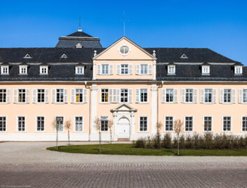 Schloss und Schlossgarten Schwetzingen - Schloss - Nordflügel / Hofkavaliersflügel - Längsbau - Von Süden - Blick vom Ehrenhof nach Norden auf die Südfassade des Nordflügels; links der Mitte im Hintergrund das Dach des Oberen Wasserwerks (Nordflügel: L-förmig, Länge x Breite Längsbau ca. 50 x 14 Meter, Querbau ca. 15 x 12 Meter; Architekt: Johann Adam Breunig (1660-1727); Fertigstellung: 1710) (aufgenommen im März 2025, um die Mittagszeit)
