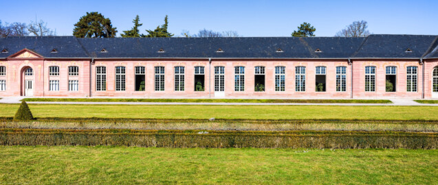 Schloss und Schlossgarten Schwetzingen - Garten - Neue Orangerie - Östlicher Seitenflügel - Blick vom Orangeriegarten auf den östlichen dreizehnachsigen Seitenflügel mit der Tür in der Mitte; einige Fenster sind zur Belüftung der eingelagerten Pflanzen geöffnet; ganz links 4 Achsen des fünfachsigen Mittelbaus, ganz rechts der dreiachsige Eckpavillon und rechts daneben die westliche Tür zum nachträglich angebauten Glashaus (Gesamter Bau: Länge ca. 171 Meter, Breite ca. 10-12 Meter; Bauzeit: 1761-1762; Architekt: Nicolas de Pigage; umfangreiche Instandsetzung: 1994-1999; Putzflächen bemalt in Freskotechnik, täuschen teilweise ein Scheinmauerwerk vor) (aufgenommen im März 2025, um die Mittagszeit) Schloss und Schlossgarten Schwetzingen - Garten - Neue Orangerie - Östlicher Seitenflügel - Blick vom Orangeriegarten auf den östlichen dreizehnachsigen Seitenflügel mit der Tür in der Mitte; einige Fenster sind zur Belüftung der eingelagerten Pflanzen geöffnet; ganz links 4 Achsen des fünfachsigen Mittelbaus, ganz rechts der dreiachsige Eckpavillon und rechts daneben die westliche Tür zum nachträglich angebauten Glashaus (Gesamter Bau: Länge ca. 171 Meter, Breite ca. 10-12 Meter; Bauzeit: 1761-1762; Architekt: Nicolas de Pigage; umfangreiche Instandsetzung: 1994-1999; Putzflächen bemalt in Freskotechnik, täuschen teilweise ein Scheinmauerwerk vor) (aufgenommen im März 2025, um die Mittagszeit)