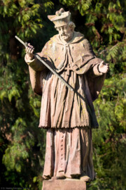 Schloss und Schlossgarten Schwetzingen - Schloss - Nahe dem Ehrenhof - Grünstreifen zwischen östlichem Ehrenhof und Leimbach - Nordostecke - Von Osten - Blick auf die Statue des Heiligen Nepomuk; die Inschrift des (nicht sichtbaren) Sockels lautet: "S. IOHANN VON NEPOMUCK / VON WENCELS WUTH BEKRIEGET / HAST AUFF DER PRAGER BRÜCK / DURCH SHWEIGEN OBSIEGET / ZUM SIEGES DENCKMAL HIER / THUT SHWETZINGEN AUFRICHTEN / DEIN BILDNIS UND SICH DIR / ZUR DIENERSCHAFT VERPFLICHTET / 1751" (zu Johannes (von) Nepomuk (um 1350-1393): böhmischer Priester und Märtyrer, 1729 heiliggesprochen, seit 1732 zweiter Ordenspatron der Jesuiten,  Brückenheiliger und Patron des Beichtgeheimnisses) (Statue ist eine Kopie, angefertigt 1927 und 1968 an diesem Ort aufgestellt; Original im Museum der Stadt Schwetzingen; Original wohl aus der Werkstatt des Hofbildhauers Paul Johann Egell (1691-1752), Datierung 1751) (aufgenommen im April 2025, am späten Vormittag)