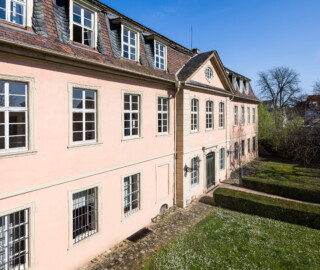Schloss und Schlossgarten Schwetzingen - Garten - Gesandtenhaus (ehemaliges Prinzenhaus) / Amtsgericht - Von Süden - Blick aus einem Fenster an der Rückseite des mittleren Pavillons des nördlichen Zirkelbaus auf die Südostfassade und das Portal des Gesandtenhauses (Nutzung: Wohnungen für Angehörige der kurfürstlichen Familie, ausländische Besucher, Nicolas de Pigage (1723-1796), Friedrich Ludwig Skell (1750-1823), Johann Michael Zeyher (1770-1843), Sterbeort von Johann Peter Hebel (1760-1826), ab 1805 Amtsgericht) (Bau: Länge x Breite: ca. 40 x 17 Meter; Bauzeit: um 1723; Architekt: unbekannt) (aufgenommen im April 2025, am späten Vormittag)