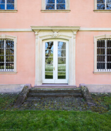Schloss und Schlossgarten Schwetzingen - Garten - Gesandtenhaus (ehemaliges Prinzenhaus) / Amtsgericht - Von Nordwest - Blick vom Gesandtenhausgarten auf das rückseitige Portal des Gesandtenhauses (Nutzung: Wohnungen für Angehörige der kurfürstlichen Familie, ausländische Besucher, Nicolas de Pigage (1723-1796), Friedrich Ludwig Skell (1750-1823), Johann Michael Zeyher (1770-1843), Sterbeort von Johann Peter Hebel (1760-1826), ab 1805 Amtsgericht) (Bau: Länge x Breite: ca. 40 x 17 Meter; Bauzeit: um 1723; Architekt: unbekannt) (aufgenommen im April 2025, am frühen Nachmittag)