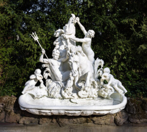Schloss und Schlossgarten Schwetzingen - Garten - Seepferdgarten - Seepferdgruppe - Von Nordwest - Blick auf die Seepferdgruppe; Tritonen (Wasserwesen der griechischen Sage, je zur Hälfte bestehend aus einem menschlichen Oberkörper und fischartigem Unterkörper mit Schwanzflosse) bekämpfen zwei wilde Wasserrösser (Bildhauer: Gabriel Grupello (1644-1730) zugeschrieben; Datierung: 1709 bis 1716; Versetzung um 1824 in den Westflügel des Karlsruher Schlossgartens; 1994 in Karlsruhe abgebaut, 1996 durch Kopie aus Epoxidharz ersetzt; Original heute im Südlichen Zirkel ausgestellt; zweite Kopie ebenso 1996 am Originalstandort im Seepferdgarten aufgestellt) (aufgenommen im April 2025, am späten Nachmittag)