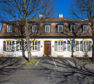 Schloss und Schlossgarten Schwetzingen - Sonstige Bauten - Palais Ysenburg (Forsthausstraße 7 und 9) - Von Nordwest - Blick von der Mauer zum Betriebshof in der Forsthausstraße nach Osten auf die Westseite des Palais Ysenburg; rechts davon (außerhalb des Bildes) befindet sich der Verbindungsbau zum Alten Forstamt (ehemalige Bewohner: Mitglieder des kurfürstlichen Hofstaats, Oberhofgärter Theodor van Wynder († 1777), bis 1778 Oberstjägermeister Graf Friedrich Wilhelm von Ysenburg-Birstein (1730-1804) und Ehefrau Caroline Gräfin von Parkstein (1762-1816), eine uneheliche Tochter von Kurfürst Carl Theodor, Oberstjägermeister Johann Theodor Maria Reichsgraf v. Waldkirch (1720–1802), Oberforstmeister Friedrich Heinrich Georg Freiherr von Drais (1758-1833), ab 1864 der Industrielle Gustav Bassermann und Ehefrau Clementine; nach 1918 Kauf durch Stadt Schwetzingen, seit 1997 in Privatbesitz) (Bau: L-formig; Länge x Breite: Nordflügel ca. 34 x 7 Meter, Westflügel ca. 21 x 13 Meter, Westflügel mit Anbau bis zum Alten Forstamt ca. 48 x 10 Meter; Geschosse: 2 (inkl. Mansardgeschoss); Bauzeiten: 1760, Verbindung zum Alten Forstamt 1775, erweitert Ende des 19. Jh., restauriert 1997; Architekt: wohl Franz Wilhelm Rabaliatti (1714–1782)) (aufgenommen im April 2025, am späten Nachmittag)