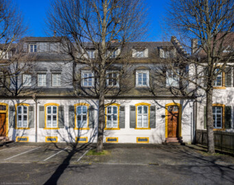 Schloss und Schlossgarten Schwetzingen - Sonstige Bauten - Palais Ysenburg (Forsthausstraße 7 und 9) - Von Nordwest - Blick von der Mauer zum Betriebshof in der Forsthausstraße nach Osten auf die Westseite des Palais Ysenburg; rechts des Zauns das Alte Forstamt (ehemalige Bewohner: Mitglieder des kurfürstlichen Hofstaats, Oberhofgärter Theodor van Wynder († 1777), bis 1778 Oberstjägermeister Graf Friedrich Wilhelm von Ysenburg-Birstein (1730-1804) und Ehefrau Caroline Gräfin von Parkstein (1762-1816), eine uneheliche Tochter von Kurfürst Carl Theodor, Oberstjägermeister Johann Theodor Maria Reichsgraf v. Waldkirch (1720–1802), Oberforstmeister Friedrich Heinrich Georg Freiherr von Drais (1758-1833), ab 1864 der Industrielle Gustav Bassermann und Ehefrau Clementine; nach 1918 Kauf durch Stadt Schwetzingen, seit 1997 in Privatbesitz) (Bau: L-formig; Länge x Breite: Nordflügel ca. 34 x 7 Meter, Westflügel ca. 21 x 13 Meter, Westflügel mit Anbau bis zum Alten Forstamt ca. 48 x 10 Meter; Geschosse: 2 (inkl. Mansardgeschoss); Bauzeiten: 1760, Verbindung zum Alten Forstamt 1775, erweitert Ende des 19. Jh., restauriert 1997; Architekt: wohl Franz Wilhelm Rabaliatti (1714–1782)) (aufgenommen im April 2025, am späten Nachmittag) Schloss und Schlossgarten Schwetzingen - Sonstige Bauten - Palais Ysenburg (Forsthausstraße 7 und 9) - Von Nordwest - Blick von der Mauer zum Betriebshof in der Forsthausstraße nach Osten auf die Westseite des Palais Ysenburg; rechts des Zauns das Alte Forstamt (ehemalige Bewohner: Mitglieder des kurfürstlichen Hofstaats, Oberhofgärter Theodor van Wynder († 1777), bis 1778 Oberstjägermeister Graf Friedrich Wilhelm von Ysenburg-Birstein (1730-1804) und Ehefrau Caroline Gräfin von Parkstein (1762-1816), eine uneheliche Tochter von Kurfürst Carl Theodor, Oberstjägermeister Johann Theodor Maria Reichsgraf v. Waldkirch (1720–1802), Oberforstmeister Friedrich Heinrich Georg Freiherr von Drais (1758-1833), ab 1864 der Industrielle Gustav Bassermann und Ehefrau Clementine; nach 1918 Kauf durch Stadt Schwetzingen, seit 1997 in Privatbesitz) (Bau: L-formig; Länge x Breite: Nordflügel ca. 34 x 7 Meter, Westflügel ca. 21 x 13 Meter, Westflügel mit Anbau bis zum Alten Forstamt ca. 48 x 10 Meter; Geschosse: 2 (inkl. Mansardgeschoss); Bauzeiten: 1760, Verbindung zum Alten Forstamt 1775, erweitert Ende des 19. Jh., restauriert 1997; Architekt: wohl Franz Wilhelm Rabaliatti (1714–1782)) (aufgenommen im April 2025, am späten Nachmittag)
