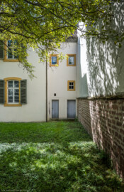 Schloss und Schlossgarten Schwetzingen - Sonstige Bauten - Altes Forstamt (Forsthausstraße 11) - Von Osten - Blick von der östlichen Gartenmauer nach Westen auf die Türen zweier Abstellräume am Nordende des Forstamts; der Baum links ist eine Echte Walnuss (Juglans regia) (Bau: Länge x Breite: ca. 22 x 14 Meter; Geschosse: 2; Fensterachsen: 7; Bauzeit: 1760; erbaut als Haus des kurfürstlichen Oberjägermeisters; Verbindung mit dem Palais Ysenburg: 1775; Architekt: unbekannt) (aufgenommen im April 2025, am Vormittag)