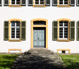 Schloss und Schlossgarten Schwetzingen - Sonstige Bauten - Altes Forstamt (Forsthausstraße 11) - Von Westen - Blick vom westlichen Weg nach Osten auf die Westfassade und den Haupteingang zum Forstamt (Bau: Länge x Breite: ca. 22 x 14 Meter; Geschosse: 2; Fensterachsen: 7; Bauzeit: 1760; erbaut als Haus des kurfürstlichen Oberjägermeisters; Verbindung mit dem Palais Ysenburg: 1775; Architekt: unbekannt) (aufgenommen im April 2025, am Nachmittag)