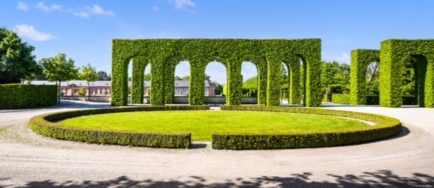 Schloss und Schlossgarten Schwetzingen - Garten - Kreisparterre - Nördliche Arkadenallee - Westseite - Von Süden - Blick auf das ovale Rasenfeld, dahinter Arkaden als nördlicher Abschluss des Kreisparterres; im Hintergrund links der Bildmitte die Neue Orangerie (aufgenommen im April 2025, am späten Nachmittag)