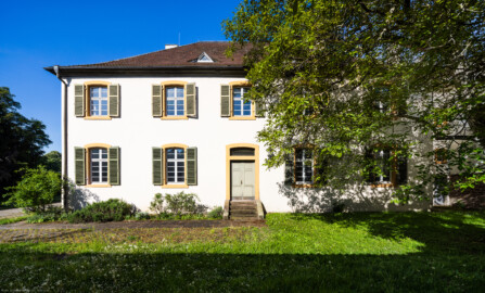Schloss und Schlossgarten Schwetzingen - Sonstige Bauten - Altes Forstamt (Forsthausstraße 11) - Von Osten - Blick von der östlichen Gartenmauer nach Westen auf die Ostfassade und den Osteingang zum Forstamt; der Baum rechts ist eine Echte Walnuss (Juglans regia) (Bau: Länge x Breite: ca. 22 x 14 Meter; Geschosse: 2; Fensterachsen: 7; Bauzeit: 1760; erbaut als Haus des kurfürstlichen Oberjägermeisters; Verbindung mit dem Palais Ysenburg: 1775; Architekt: unbekannt) (aufgenommen im April 2025, am Vormittag)