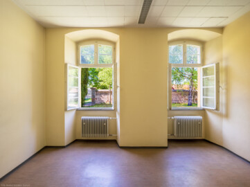 Schloss und Schlossgarten Schwetzingen - Sonstige Bauten - Altes Forstamt (Forsthausstraße 11) - Von innen - Erdgeschoss - Büro / Südwestliches Zimmer - Von Osten - Blick nach Westen in das Zimmer und auf den Garten; die Mauer gehört zur alten Begrenzungsmauer um Teile des Schlossgartens; dahinter liegt der  Betriebshof (Bau: Länge x Breite: ca. 22 x 14 Meter; Geschosse: 2; Fensterachsen: 7; Bauzeit: 1760; erbaut als Haus des kurfürstlichen Oberjägermeisters; Verbindung mit dem Palais Ysenburg: 1775; Architekt: unbekannt) (aufgenommen im April 2025, um die Mittagszeit)