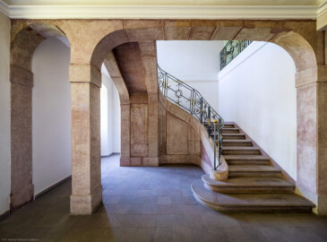 Schloss und Schlossgarten Schwetzingen - Sonstige Bauten - Altes Forstamt (Forsthausstraße 11) - Von innen - Treppenhaus - Erdgeschoss - Von Norden - Zentraler Blick nach Süden in das Treppenhaus und auf die Treppe aus Sandstein mit dem schmiedeeisernen Geländer; im Vordergrund ganz links die (nicht sichtbare) östliche Eingangstür; im Vordergrund ganz rechts der (nicht sichtbare) Durchgang in den westlichen Teil des Erdgeschosses (Bau: Länge x Breite: ca. 22 x 14 Meter; Geschosse: 2; Fensterachsen: 7; Bauzeit: 1760; erbaut als Haus des kurfürstlichen Oberjägermeisters; Verbindung mit dem Palais Ysenburg: 1775; Architekt: unbekannt) (aufgenommen im April 2025, am frühen Nachmittag)