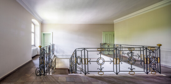 Schloss und Schlossgarten Schwetzingen - Sonstige Bauten - Altes Forstamt (Forsthausstraße 11) - Von innen - Treppenhaus - Obergeschoss - Von Norden - Blick nach Süden in das Treppenhaus und auf die Treppe aus Sandstein mit dem schmiedeeisernen Geländer; die Tür links führt in eine Wohnung, die Tür rechts in den Speicher bzw. den Dachstuhl (Bau: Länge x Breite: ca. 22 x 14 Meter; Geschosse: 2; Fensterachsen: 7; Bauzeit: 1760; erbaut als Haus des kurfürstlichen Oberjägermeisters; Verbindung mit dem Palais Ysenburg: 1775; Architekt: unbekannt) (aufgenommen im Juni 2025, am Nachmittag)