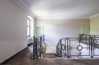 Schloss und Schlossgarten Schwetzingen - Sonstige Bauten - Altes Forstamt (Forsthausstraße 11) - Von innen - Treppenhaus - Obergeschoss - Von Norden - Blick nach Süden in das Treppenhaus und auf die Treppe aus Sandstein mit dem schmiedeeisernen Geländer; die Tür links führt in eine Wohnung, die Tür rechts in den Speicher bzw. den Dachstuhl (Bau: Länge x Breite: ca. 22 x 14 Meter; Geschosse: 2; Fensterachsen: 7; Bauzeit: 1760; erbaut als Haus des kurfürstlichen Oberjägermeisters; Verbindung mit dem Palais Ysenburg: 1775; Architekt: unbekannt) (aufgenommen im Juni 2025, am Nachmittag)
