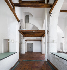 Schloss und Schlossgarten Schwetzingen - Sonstige Bauten - Oberes Wasserwerk - Wasserturm - Von innen - Obergeschoss / Cafeteria / Kantine - Von Westen - Blick von der Theke der Cafeteria nach Osten auf den Eingangsbereich; Wände und mittige Pfeiler sind "gotisch" bzw. spitzbogenartig gestaltet; das Gitter aus Balken in der Bildmitte ist eine kleine Zwischenebene zum Aufstieg in den Dachstuhl über Eisenleitern; rechts eine der vier Leitungen (Steigleitung? / Fallleitung?) von der Brunnenstube zu den Wasserbehältern im Dachgeschoss; eiserne Anker in den Pfeilern und Holzbalken dienten wohl als Zwischenebenen zur Lagerung (Gesamte Anlage Brunnenstube, Pumpenstube, Räderwerk, Wasserturm und Kühlhaus): Länge x Breite: ca. 30 x 29 Meter, Wasserturm: Länge x Breite: ca. 14 x 14 Meter, Firsthöhe ca. 24 Meter; Bauzeit Anlage: um 1774, Gesamtinstandsetzung: 1994–2000; Architekt: Nicolas de Pigage, Brunnenmeister: Thomas Breuer) (aufgenommen im Juni 2025, am Nachmittag)