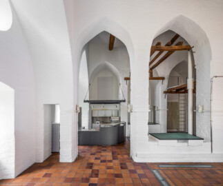 Schloss und Schlossgarten Schwetzingen - Sonstige Bauten - Oberes Wasserwerk - Wasserturm - Von innen - Obergeschoss / Cafeteria / Kantine - Von Süden - Blick nach Norden auf die Theke der Cafeteria; Wände und mittige Pfeiler sind "gotisch" bzw. spitzbogenartig gestaltet; rechts eine Eisenleiter zum Aufstieg auf eine kleine Zwischenebene, die zum Dachstuhl über eine weitere Eisenleiter führt; rechts eine der vier Leitungen (Steigleitung? / Fallleitung?) von der Brunnenstube zu den Wasserbehältern im Dachgeschoss; eiserne Anker in den Wänden und Pfeilern und Holzbalken dienten wohl als Zwischenebenen zur Lagerung (Gesamte Anlage Brunnenstube, Pumpenstube, Räderwerk, Wasserturm und Kühlhaus): Länge x Breite: ca. 30 x 29 Meter, Wasserturm: Länge x Breite: ca. 14 x 14 Meter, Firsthöhe ca. 24 Meter; Bauzeit Anlage: um 1774, Gesamtinstandsetzung: 1994–2000; Architekt: Nicolas de Pigage, Brunnenmeister: Thomas Breuer) (aufgenommen im Juni 2025, am frühen Nachmittag)