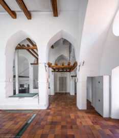 Schloss und Schlossgarten Schwetzingen - Sonstige Bauten - Oberes Wasserwerk - Wasserturm - Von innen - Obergeschoss / Cafeteria / Kantine - Von Süden - Blick nach Norden auf eine Eisenleiter zum Aufstieg auf eine kleine Zwischenebene, die zum Dachstuhl über eine weitere Eisenleiter führt; links die Theke der Cafeteria; Wände und mittige Pfeiler sind "gotisch" bzw. spitzbogenartig gestaltet; links eine der vier Leitungen (Steigleitung? / Fallleitung?) von der Brunnenstube zu den Wasserbehältern im Dachgeschoss; eiserne Anker in den Wänden und Pfeilern und Holzbalken dienten wohl als Zwischenebenen zur Lagerung (Gesamte Anlage Brunnenstube, Pumpenstube, Räderwerk, Wasserturm und Kühlhaus): Länge x Breite: ca. 30 x 29 Meter, Wasserturm: Länge x Breite: ca. 14 x 14 Meter, Firsthöhe ca. 24 Meter; Bauzeit Anlage: um 1774, Gesamtinstandsetzung: 1994–2000; Architekt: Nicolas de Pigage, Brunnenmeister: Thomas Breuer) (aufgenommen im Juni 2025, am Nachmittag)