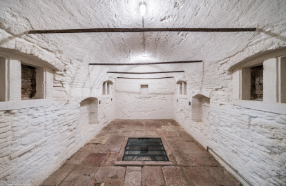Schloss und Schlossgarten Schwetzingen - Sonstige Bauten - Oberes Wasserwerk - Kühlhaus - Von innen - Wildbretkeller - Von Süden - Blick vom Eingang zum Wildbretkeller nach Norden in den gewölbten Raum; der Wildbretkeller diente dem Abhängen von Wild an den eisernen Stangen und zur Lagerung von Lebensmitteln; am Fußboden in der Mitte ein großes Loch, um den darunter liegenden zugangslosen Eiskeller mit Eisblöcken zu befüllen (Gesamte Anlage Brunnenstube, Pumpenstube, Räderwerk, Wasserturm und Kühlhaus): Länge x Breite: ca. 30 x 29 Meter, Kühlhaus: Länge x Breite: ca. 14 x 13 Meter, Firsthöhe ca. 14 Meter, Kellertiefe ca. 3 Meter; Bauzeit Anlage: um 1774, Gesamtinstandsetzung: 1994–2000; Architekt: Nicolas de Pigage, Brunnenmeister: Thomas Breuer) (aufgenommen im Juni 2025, am Nachmittag) Schloss und Schlossgarten Schwetzingen - Sonstige Bauten - Oberes Wasserwerk - Kühlhaus - Von innen - Wildbretkeller - Von Süden - Blick vom Eingang zum Wildbretkeller nach Norden in den gewölbten Raum; der Wildbretkeller diente dem Abhängen von Wild an den eisernen Stangen und zur Lagerung von Lebensmitteln; am Fußboden in der Mitte ein großes Loch, um den darunter liegenden zugangslosen Eiskeller mit Eisblöcken zu befüllen (Gesamte Anlage Brunnenstube, Pumpenstube, Räderwerk, Wasserturm und Kühlhaus): Länge x Breite: ca. 30 x 29 Meter, Kühlhaus: Länge x Breite: ca. 14 x 13 Meter, Firsthöhe ca. 14 Meter, Kellertiefe ca. 3 Meter; Bauzeit Anlage: um 1774, Gesamtinstandsetzung: 1994–2000; Architekt: Nicolas de Pigage, Brunnenmeister: Thomas Breuer) (aufgenommen im Juni 2025, am Nachmittag)