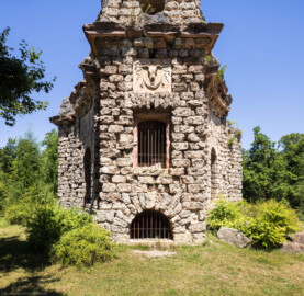 Schloss und Schlossgarten Schwetzingen - Garten - Merkurtempel - Von außen - Von Süden - Blick auf die schmale Südseite des Merkurtempels, als Ruine gebaut; das Mauerwerk besteht aus Tuffsteinquadern, die Gesimse aus Sandsteinblöcken, das Relief aus wetterfestem Marmorstuck; das oberste Feld zeigt ein Bukranion mit einer Girlande über den Hörnern, in der Mitte ein Fenster des Treppenaufgangs, unten ein Rundbogenfenster des Untergeschosses (Architekt: Nicolas de Pigage (1723-1796); Bauzeit: 1784-1792, Restaurierung: 2008–2013; Abmessungen: Grundfläche des Sechsecks Länge x Breite ca. 14 x 12 Meter, Länge konkave Portalseiten ca. 10 Meter, Tiefe Kabinettseiten ca. 3,5 Meter, Durchmesser Tambour ca. 6,5 Meter, Höhe ca. 25 Meter, 4 Geschosse) (aufgenommen im Juni 2025, am frühen Nachmittag)