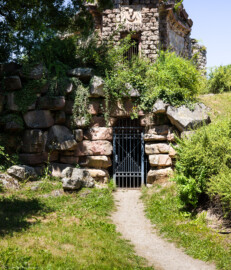 Schloss und Schlossgarten Schwetzingen - Garten - Merkurtempel - Von außen - Von Süden - Blick auf eine vergitterte Tür, dahinter ein tonnengewölbter Gang, der zum zentralen Innenraum im Untergeschoss führt (Architekt: Nicolas de Pigage (1723-1796); Bauzeit: 1784-1792, Restaurierung: 2008–2013; Abmessungen: Grundfläche des Sechsecks Länge x Breite ca. 14 x 12 Meter, Länge konkave Portalseiten ca. 10 Meter, Tiefe Kabinettseiten ca. 3,5 Meter, Durchmesser Tambour ca. 6,5 Meter, Höhe ca. 25 Meter, 4 Geschosse) (aufgenommen im Juni 2025, am frühen Nachmittag)