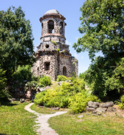 Schloss und Schlossgarten Schwetzingen - Garten - Merkurtempel - Von außen - Von Süden - Blick nach Norden auf den Merkurtempel, als Ruine gebaut; etwas links unterhalb der Bildmitte eine vergitterte Tür, dahinter der Zugang zum Untergeschoss, rechts führt ein Fußweg zum östlichen Eingang (Architekt: Nicolas de Pigage (1723-1796); Bauzeit: 1784-1792, Restaurierung: 2008–2013; Abmessungen: Grundfläche des Sechsecks Länge x Breite ca. 14 x 12 Meter, Länge konkave Portalseiten ca. 10 Meter, Tiefe Kabinettseiten ca. 3,5 Meter, Durchmesser Tambour ca. 6,5 Meter, Höhe ca. 25 Meter, 4 Geschosse) (aufgenommen im Juni 2025, am Nachmittag)