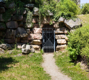 Schloss und Schlossgarten Schwetzingen - Garten - Merkurtempel - Von außen - Von Süden - Blick auf eine vergitterte Tür, dahinter ein tonnengewölbter Gang, der zum zentralen Innenraum im Untergeschoss führt (Architekt: Nicolas de Pigage (1723-1796); Bauzeit: 1784-1792, Restaurierung: 2008–2013; Abmessungen: Grundfläche des Sechsecks Länge x Breite ca. 14 x 12 Meter, Länge konkave Portalseiten ca. 10 Meter, Tiefe Kabinettseiten ca. 3,5 Meter, Durchmesser Tambour ca. 6,5 Meter, Höhe ca. 25 Meter, 4 Geschosse) (aufgenommen im Juni 2025, am frühen Nachmittag) Schloss und Schlossgarten Schwetzingen - Garten - Merkurtempel - Von außen - Von Süden - Blick auf eine vergitterte Tür, dahinter ein tonnengewölbter Gang, der zum zentralen Innenraum im Untergeschoss führt (Architekt: Nicolas de Pigage (1723-1796); Bauzeit: 1784-1792, Restaurierung: 2008–2013; Abmessungen: Grundfläche des Sechsecks Länge x Breite ca. 14 x 12 Meter, Länge konkave Portalseiten ca. 10 Meter, Tiefe Kabinettseiten ca. 3,5 Meter, Durchmesser Tambour ca. 6,5 Meter, Höhe ca. 25 Meter, 4 Geschosse) (aufgenommen im Juni 2025, am frühen Nachmittag)