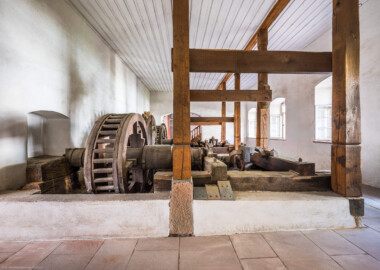 Schloss und Schlossgarten Schwetzingen - Sonstige Bauten - Oberes Wasserwerk - Pumpenstube - Von innen - Von Osten - Blick von der Ostwand des Pumpenhauses nach Westen in den Raum und auf die Pumpenanlage; auf der linken Seite die vier Holzräder und vier Wellen der Pumpen, auf der rechten Seite die zwei Kurbelwellen und zwei Pumpenschächte mit den sieben Hubkolbenpumpen; links hinter der Wand befinden sich die beiden Wasserräder, angetrieben durch den Leimbach (Gesamte Anlage Brunnenstube, Pumpenstube, Räderwerk, Wasserturm und Kühlhaus): Länge x Breite: ca. 30 x 29 Meter, Pumpenstube: Länge x Breite: ca. 13 x 9 Meter; Bauzeit Anlage: um 1774, Gesamtinstandsetzung: 1994–2000; Architekt: Nicolas de Pigage, Brunnenmeister: Thomas Breuer) (aufgenommen im Juli 2025, am späten Vormittag)