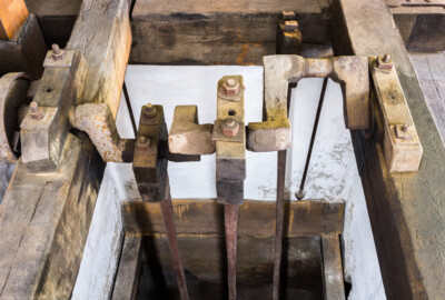 Schloss und Schlossgarten Schwetzingen - Sonstige Bauten - Oberes Wasserwerk - Pumpenstube - Von innen - Östliche Räder und Pumpen - Von Osten - Blick schräg nach unten in den östlichen Pumpenschacht (Länge x Breite x Tiefe ca. 2,5 x 2 x 4 Meter), auf die Kurbelwelle für die drei Hubkolbenpumpen und auf die drei Kolbenstangen (Länge ca. 2,9 Meter); die rechte Kolbenstange ist aus der Kurbelwelle ausgehängt und nach hinten angelehnt (Gesamte Anlage Brunnenstube, Pumpenstube, Räderwerk, Wasserturm und Kühlhaus): Länge x Breite: ca. 30 x 29 Meter, Pumpenstube: Länge x Breite: ca. 13 x 9 Meter; Bauzeit Anlage: um 1774, Gesamtinstandsetzung: 1994–2000; Architekt: Nicolas de Pigage, Brunnenmeister: Thomas Breuer) (aufgenommen im Juli 2025, am frühen Nachmittag)