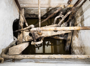 Schloss und Schlossgarten Schwetzingen - Sonstige Bauten - Oberes Wasserwerk - Pumpenstube - Von innen - Westliche Räder und Pumpen - Von Westen - Blick schräg nach unten in den westlichen Pumpenschacht (Länge x Breite x Tiefe ca. 2,5 x 2 x 4 Meter); links die Verbindung zu den Brunnen; im schräg verlaufenden Brett in der Mitte befinden sich die vier Hubkolbenpumpen aus Messing, darüber die vier Kolbenstangen mit einer Länge von ca. 2,9 Meter; unterhalb der linken beiden und oberhalb der rechten beiden Pumpen der Ansatz der Steigleitungen zu den Wasserbehältern im Wasserturm; unten im Bild sind Reflexion der hellen Bretter der Decke zu sehen (Gesamte Anlage Brunnenstube, Pumpenstube, Räderwerk, Wasserturm und Kühlhaus): Länge x Breite: ca. 30 x 29 Meter, Pumpenstube: Länge x Breite: ca. 13 x 9 Meter; Bauzeit Anlage: um 1774, Gesamtinstandsetzung: 1994–2000; Architekt: Nicolas de Pigage, Brunnenmeister: Thomas Breuer) (aufgenommen im Juli 2025, am späten Nachmittag) Schloss und Schlossgarten Schwetzingen - Sonstige Bauten - Oberes Wasserwerk - Pumpenstube - Von innen - Westliche Räder und Pumpen - Von Westen - Blick schräg nach unten in den westlichen Pumpenschacht (Länge x Breite x Tiefe ca. 2,5 x 2 x 4 Meter); links die Verbindung zu den Brunnen; im schräg verlaufenden Brett in der Mitte befinden sich die vier Hubkolbenpumpen aus Messing, darüber die vier Kolbenstangen mit einer Länge von ca. 2,9 Meter; unterhalb der linken beiden und oberhalb der rechten beiden Pumpen der Ansatz der Steigleitungen zu den Wasserbehältern im Wasserturm; unten im Bild sind Reflexion der hellen Bretter der Decke zu sehen (Gesamte Anlage Brunnenstube, Pumpenstube, Räderwerk, Wasserturm und Kühlhaus): Länge x Breite: ca. 30 x 29 Meter, Pumpenstube: Länge x Breite: ca. 13 x 9 Meter; Bauzeit Anlage: um 1774, Gesamtinstandsetzung: 1994–2000; Architekt: Nicolas de Pigage, Brunnenmeister: Thomas Breuer) (aufgenommen im Juli 2025, am späten Nachmittag)