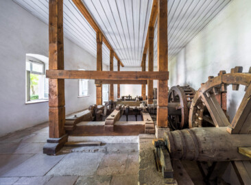Schloss und Schlossgarten Schwetzingen - Sonstige Bauten - Oberes Wasserwerk - Pumpenstube - Von innen - Von Westen - Blick von der Westwand des Pumpenhauses nach Osten in den Raum und auf die Pumpenanlage; auf der recthen Seite die vier Holzräder und vier Wellen der Pumpen, auf der linken Seite die zwei Kurbelwellen und zwei Pumpenschächte mit den sieben Hubkolbenpumpen; rechts hinter der Wand befinden sich die beiden Wasserräder, angetrieben durch den Leimbach (Gesamte Anlage Brunnenstube, Pumpenstube, Räderwerk, Wasserturm und Kühlhaus): Länge x Breite: ca. 30 x 29 Meter, Pumpenstube: Länge x Breite: ca. 13 x 9 Meter; Bauzeit Anlage: um 1774, Gesamtinstandsetzung: 1994–2000; Architekt: Nicolas de Pigage, Brunnenmeister: Thomas Breuer) (aufgenommen im Juli 2025, am Nachmittag)